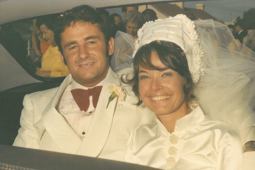 A vintage photograph of a couple in the back of their car on their wedding day