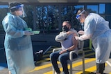 A masked man gets vaccinated in a car park.