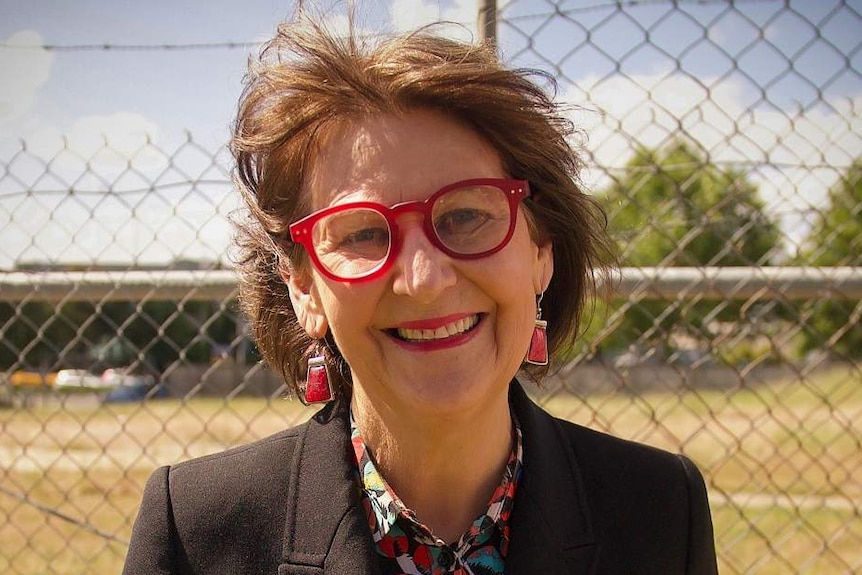 Bronwyn Pike smiles as she stands in front of a grassy field and fence.