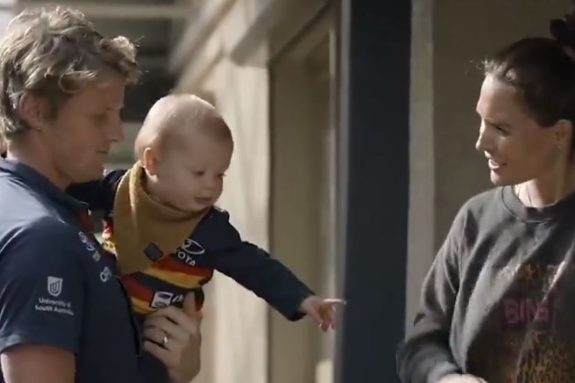 Rory Sloane holds his son, who is wearing an Adelaide jersey, while speaking to his wife Belinda