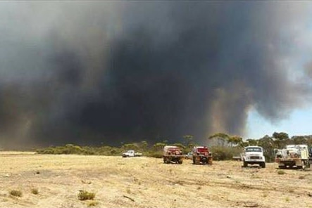 Thick black smoke rises over a paddock on which firefighting trucks are parked at Cascades, near Esperance.