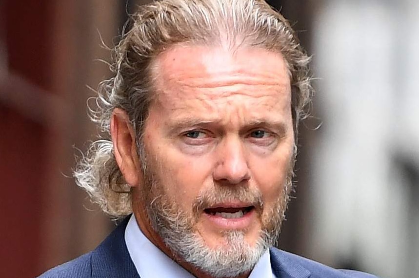 Craig McLachlan, dressed in a blue suit and yellow tie, walks down a street in Sydney with a woman by his side.