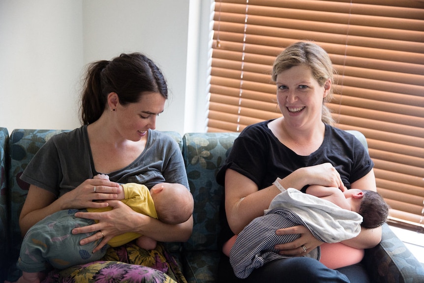 Two mothers sitting side-by-side with their babies.