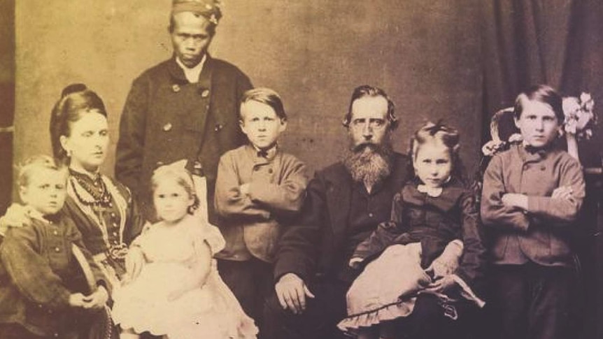 An historic black and white family portrait showing a white man, women and five children sitting with an Asian servant standing.