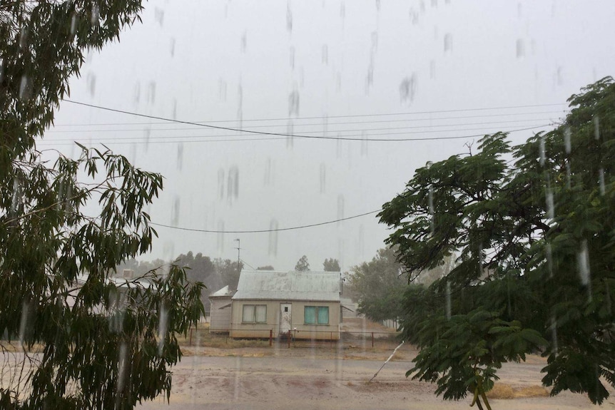 Large raindrops falling in the foreground with a small house in the background.