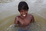 A young Indigenous boy sitting in a river.