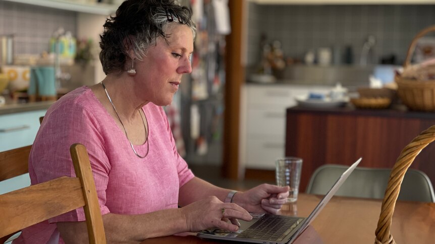 a woman wearing a pink jumper sits at the kitchen table