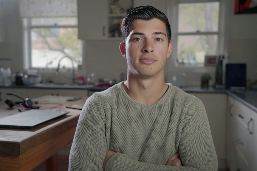 A young man with his arms crossed in a kitchen.