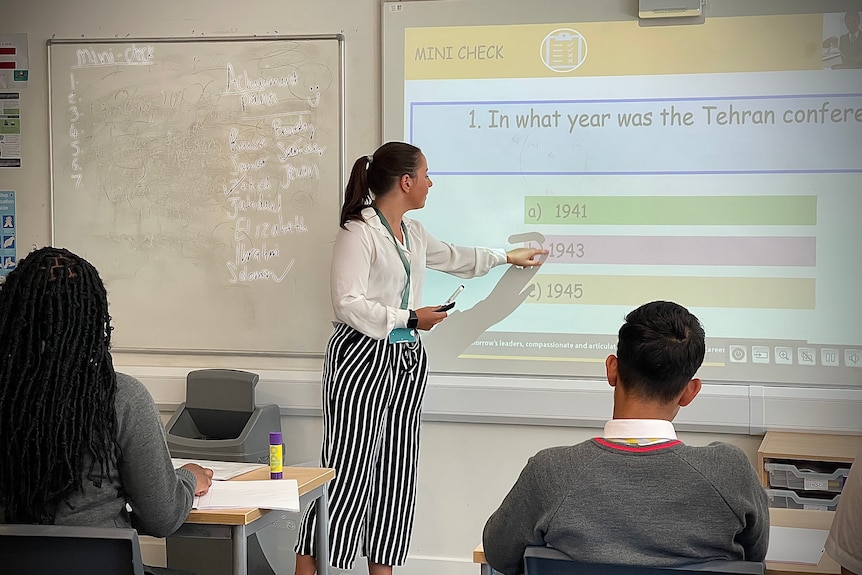 A teacher points at a whiteboard in c classroom.