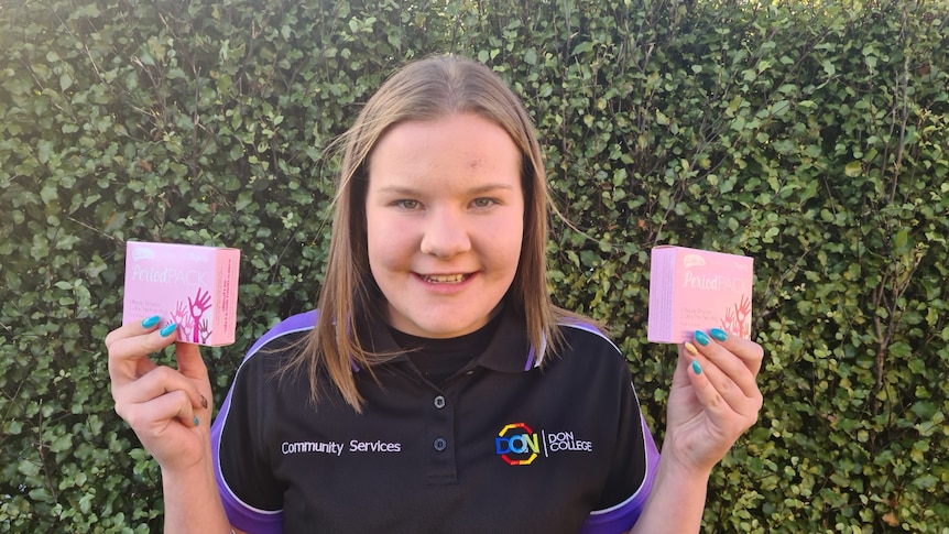 Emm Johnston holds two pink boxes with the words "period packs" written on them
