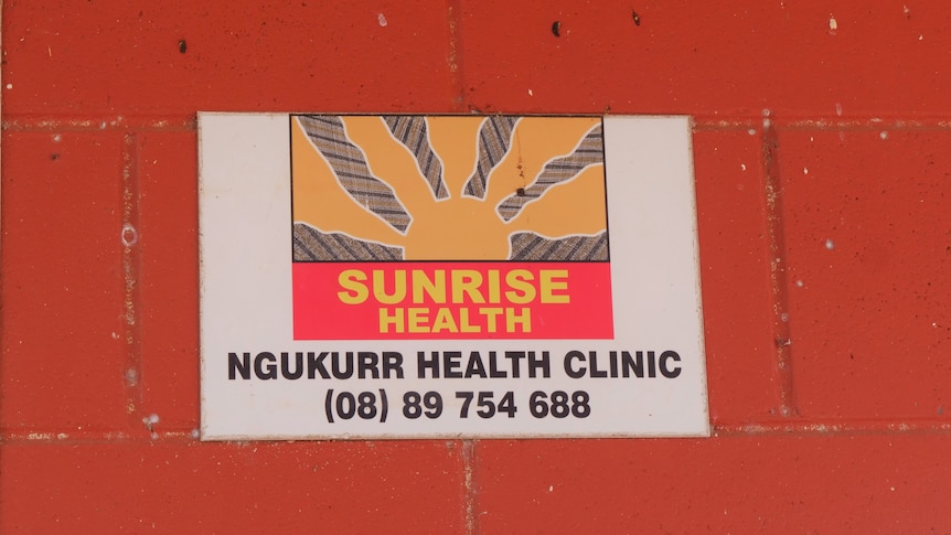 A health service logo of a sunrise on a sign on a red wall