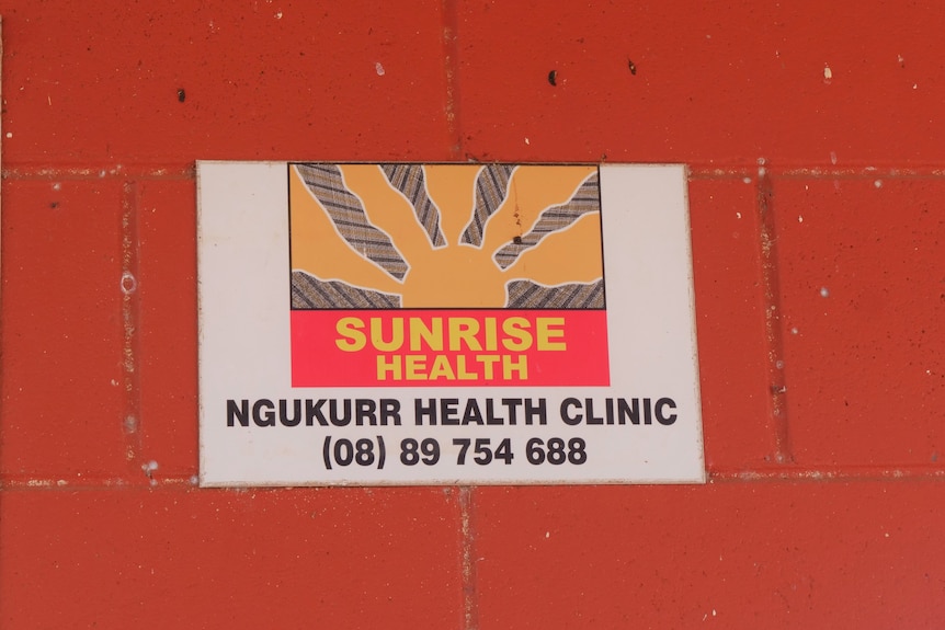 A health service logo of a sunrise on a sign on a red wall