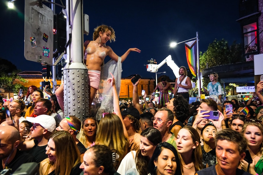 Une jeune femme se tient élevée sur un poteau électrique à hauteur d'épaule au-dessus d'une foule de fêtards