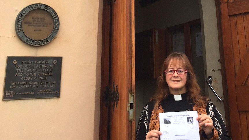 A priest stands in church doorway holding an A4 paper in her hands