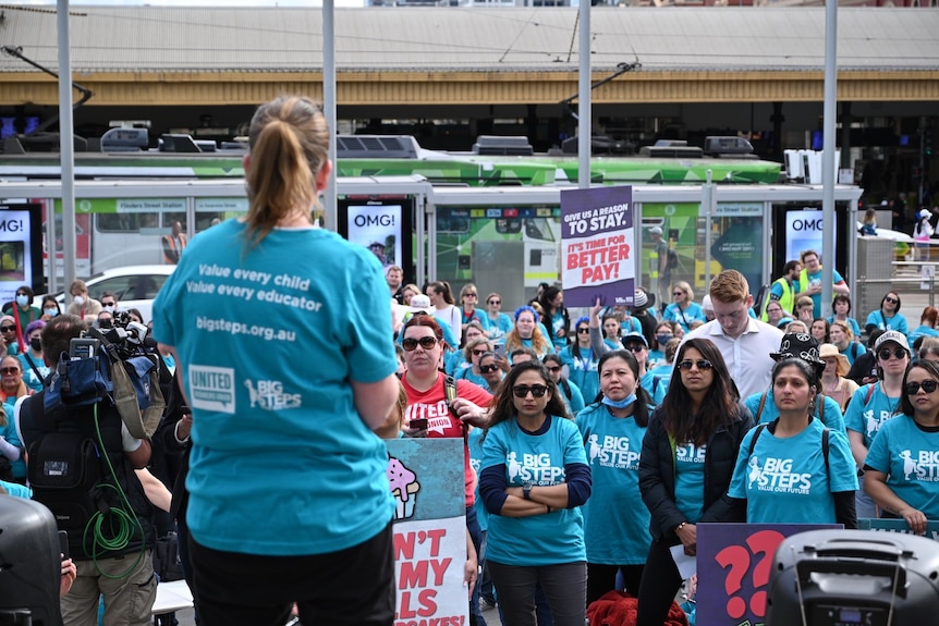 a group of people wearing blue t-shirts and holding signs. there is a tram in the background.