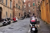 A street is lined by scooters and brick buildings.