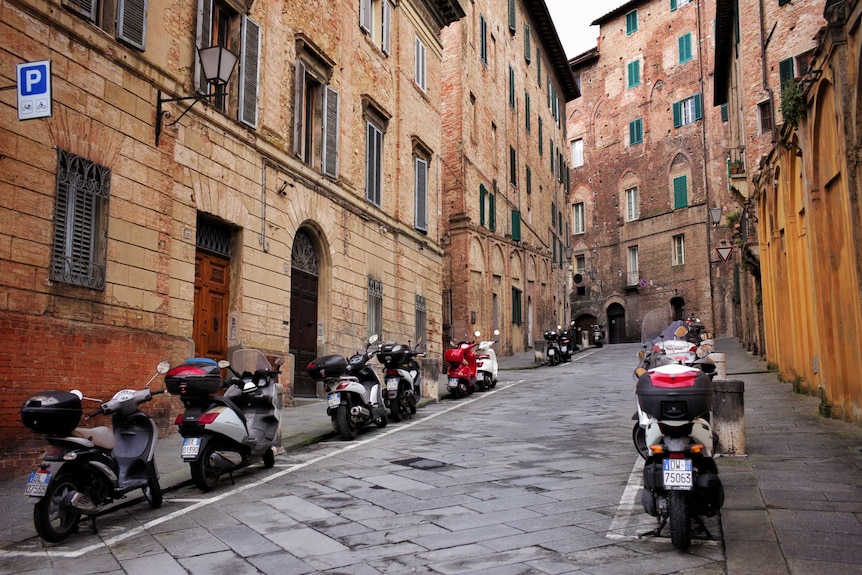 A street is lined by scooters and brick buildings.