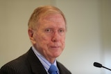 Michael Kirby in a suit standing in front of a microphone