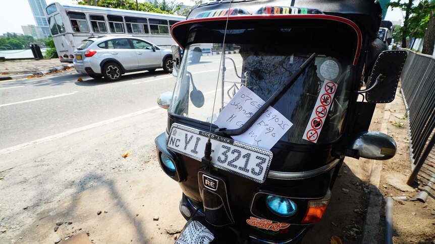 A close up of a tuk tuk with a name and number scrawled on a piece of paper attached to the windscreen.