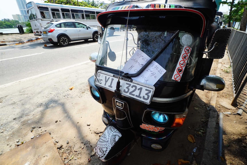 A close up of a tuk tuk with a name and number scrawled on a piece of paper attached to the windscreen.