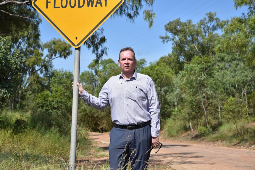A man stands near a floodway sign. 