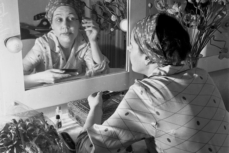 A 1940s black and white photo of an actress applying make-up, with a mirror.
