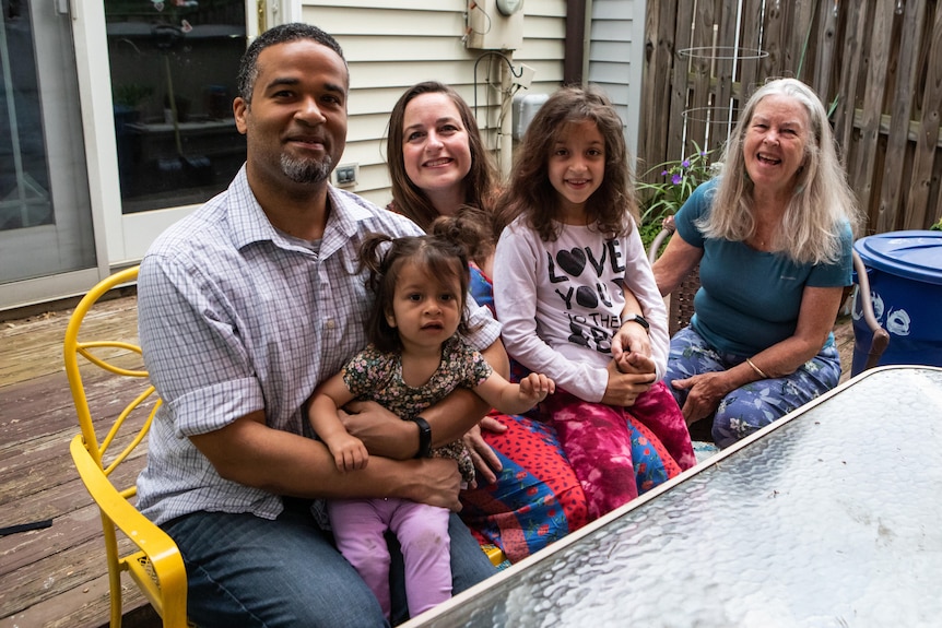 A couple sit at an outdoor table with a toddler and seven-year-old daughter