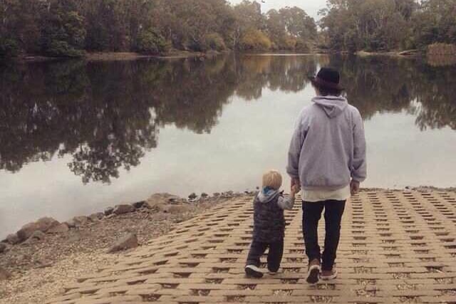 A dad holds his young son's hand as they walk down to the water.
