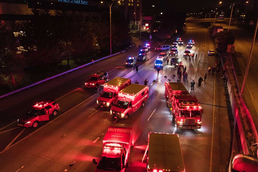 Emergency vehicles block an eight-lane highway at night, with flashing lights, with police on road.