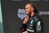 Lewis Hamilton smiles and squints into the sun while holding a microphone