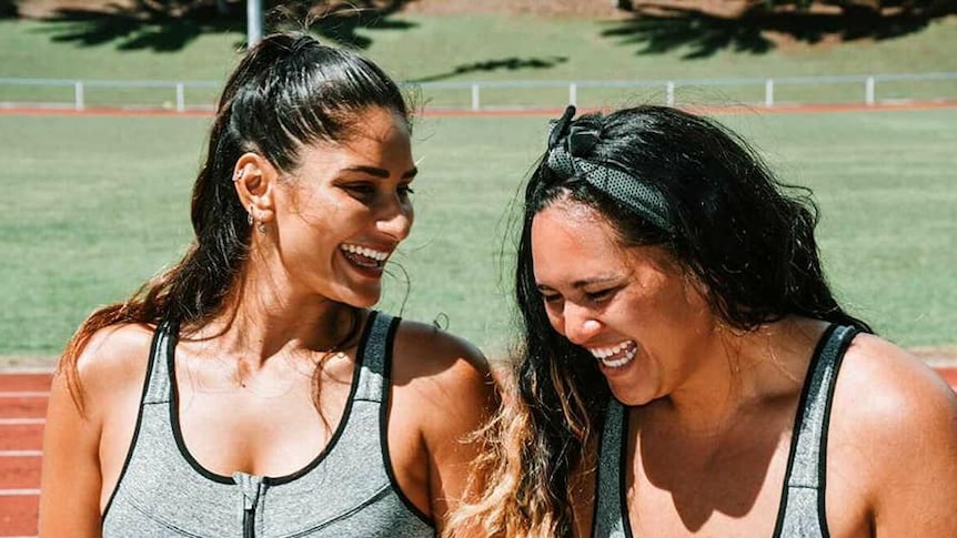 two Cook Islander women wearing sports bra laugh with each other