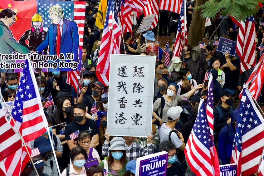 A large crowd holds numerous American flags and pro-Donald Trump banners while a placard in the middle has Chinese characters.