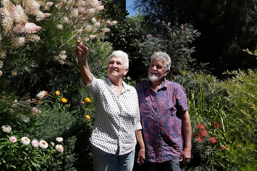 A couple smile while looking at flowers in their garden