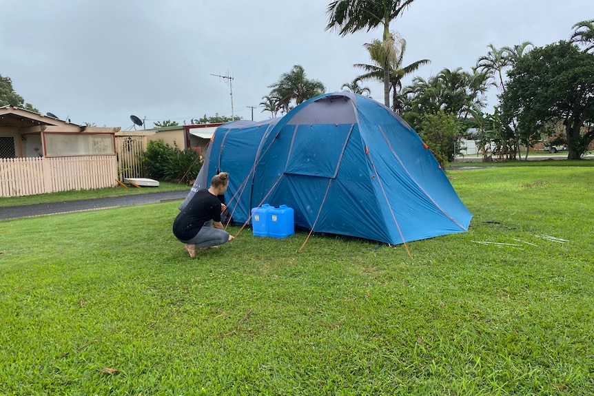 Woman setting up a blue tent on the lawn.