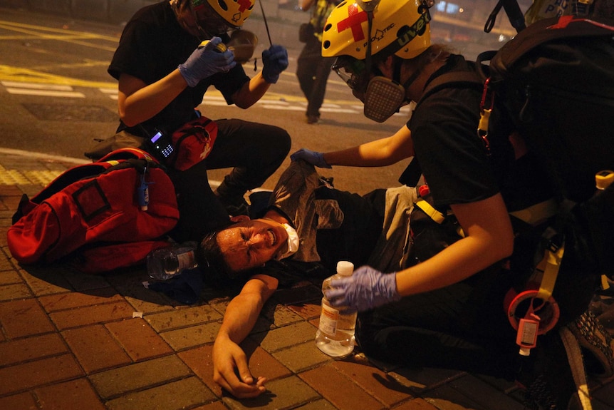 Two medical workers help a protester lying on the ground in pain from tear gas fired by policemen on a street in Hong Kong