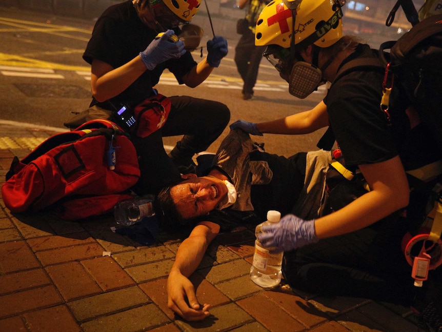 Two medical workers help a protester lying on the ground in pain from tear gas fired by policemen on a street in Hong Kong