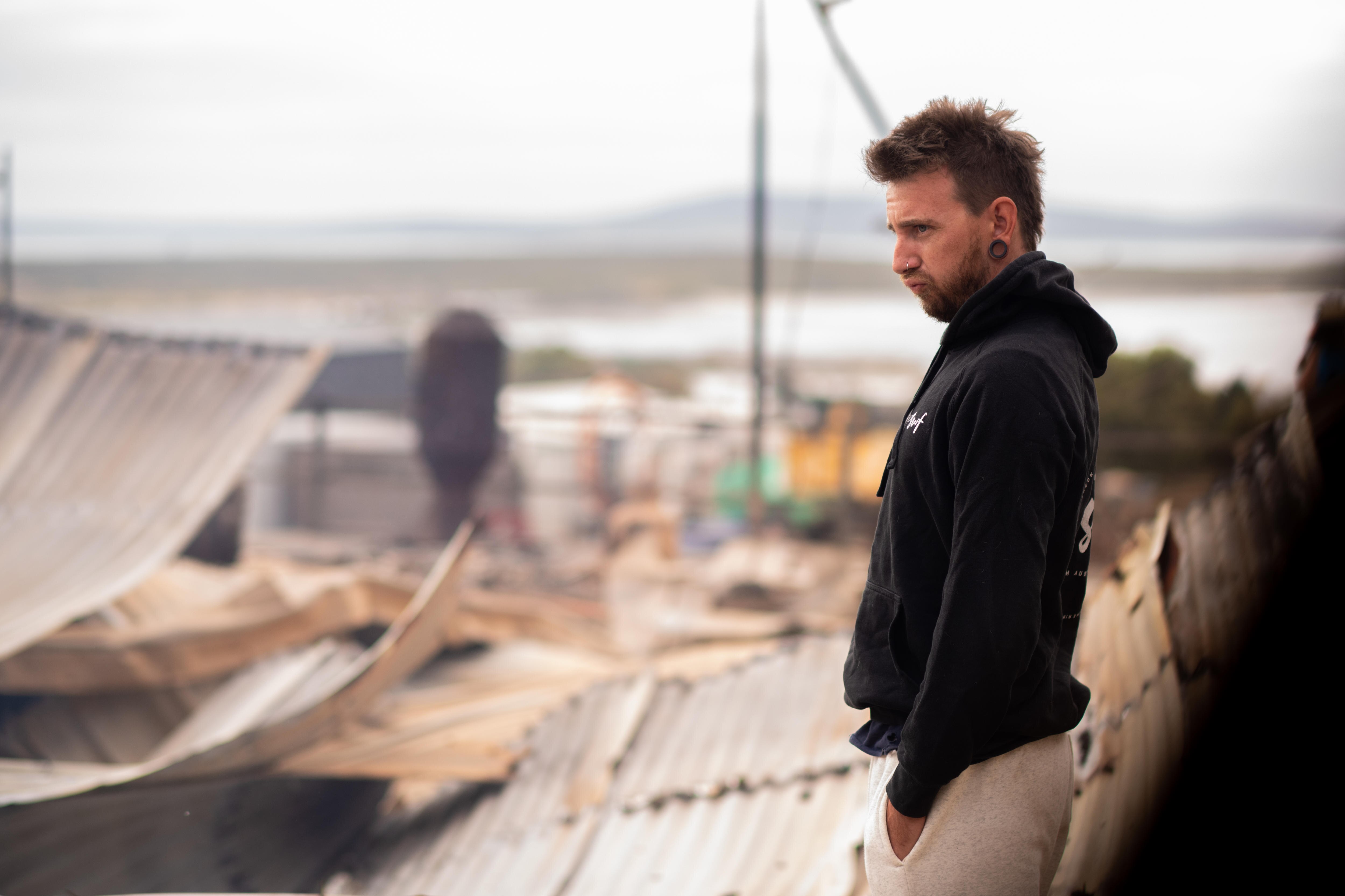 The side profile of a man standing in front of a flattened home, with a serious expression