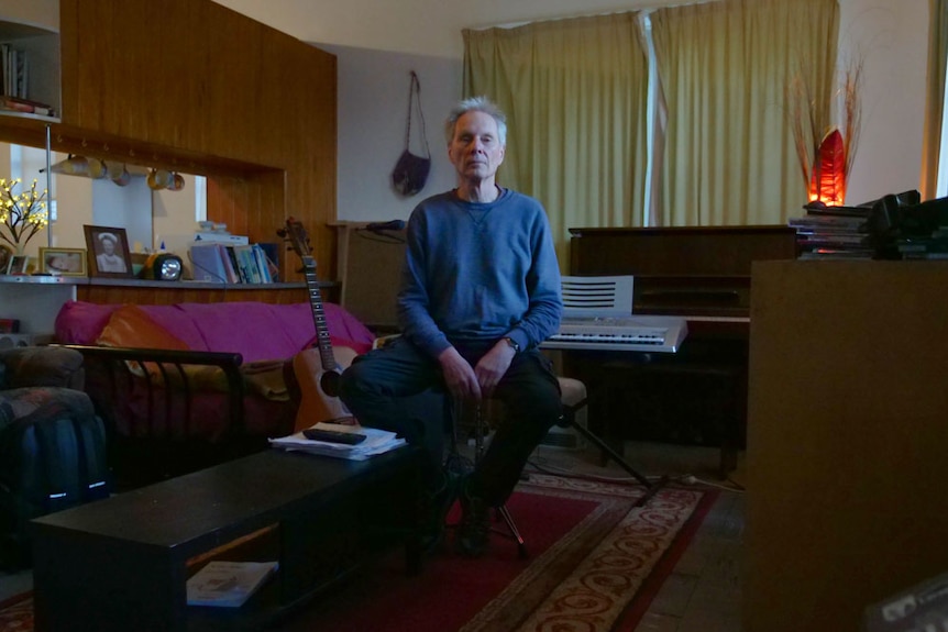 A man sitting in front of a keyboard and guitar in a living room.