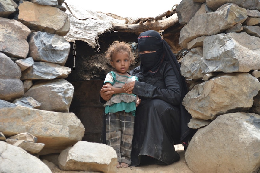 A woman wearing black traditional clothes hugs a small girl in the doorway of a stone building.