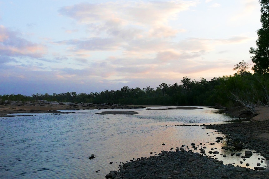 A sunset over a rocky tree-lined creek