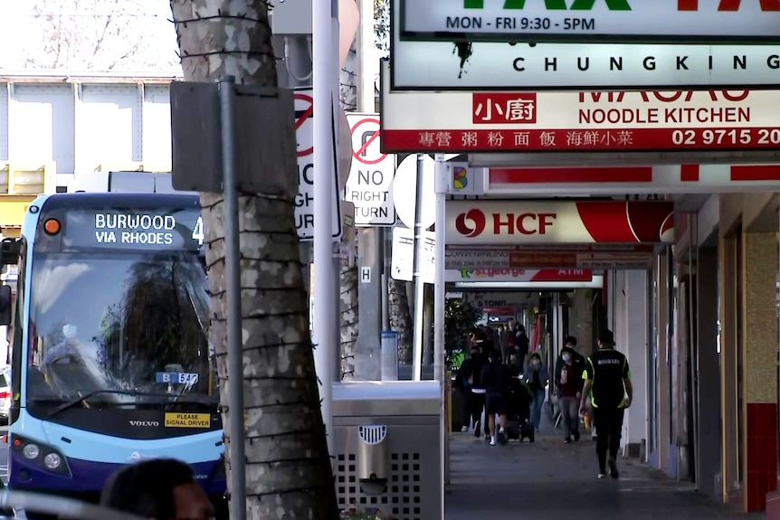 A bus departs from a stop outside shops on Burwood Road.