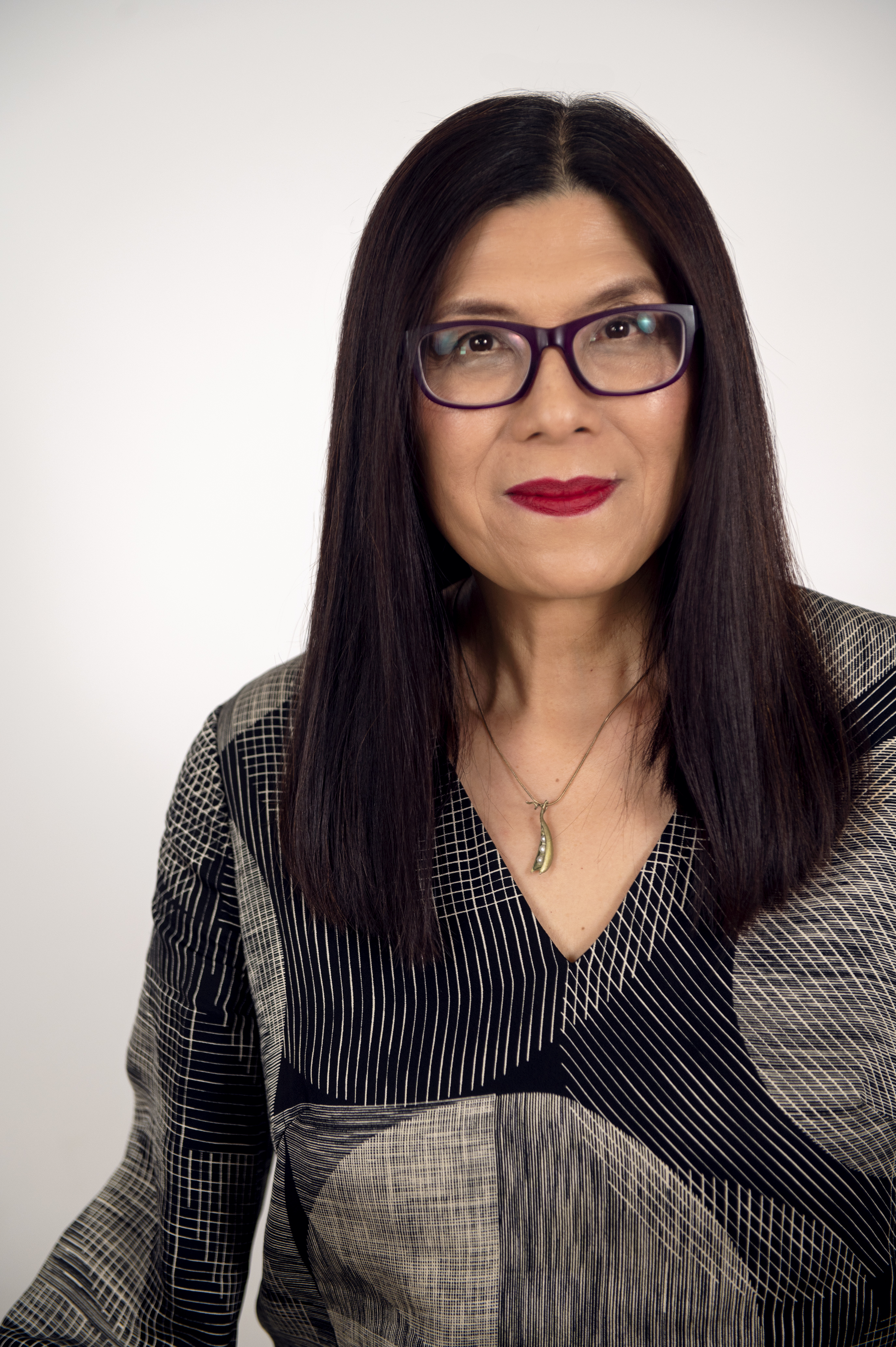 A portrait of a middle-aged Asian Australian woman with long dark hair, wearing glasses and a patterned dark shirt.