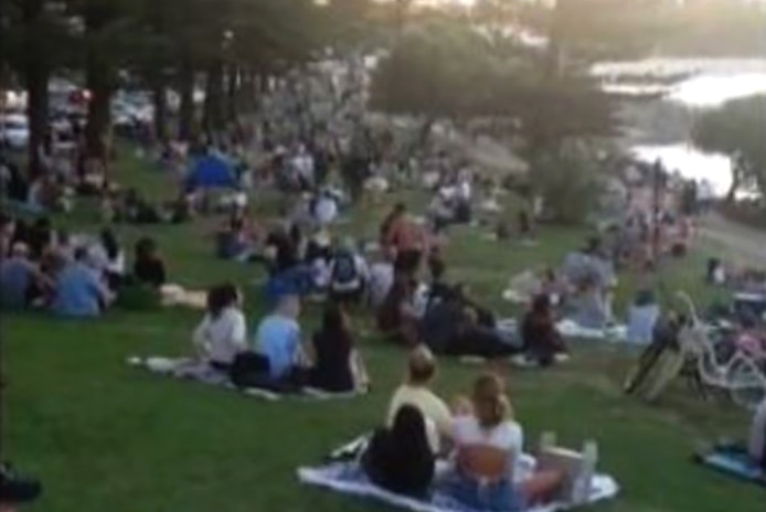 A large number of people sitting on a waterfront headland