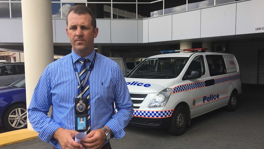 Man with police badge in front of marked police van.