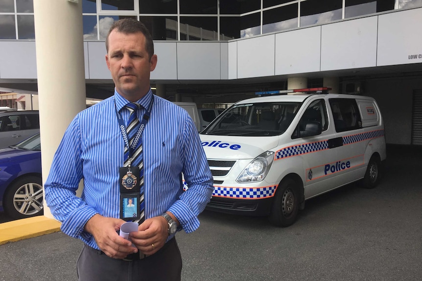 Man with police badge in front of marked police van