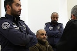 Mohammad El Halabi sits in court flanked by security officials.
