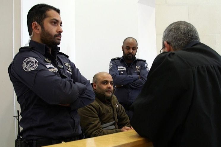 Mohammad El Halabi sits in court flanked by security officials.