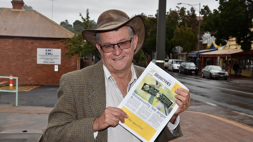A man in an akubra stands on a street holding a newspaper