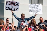 Milo Yiannopoulos holds up signs to a crowd of supporters on a university campus.