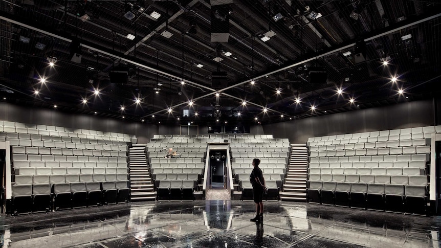 An empty theatre, grey seats, lights, black reflective stage